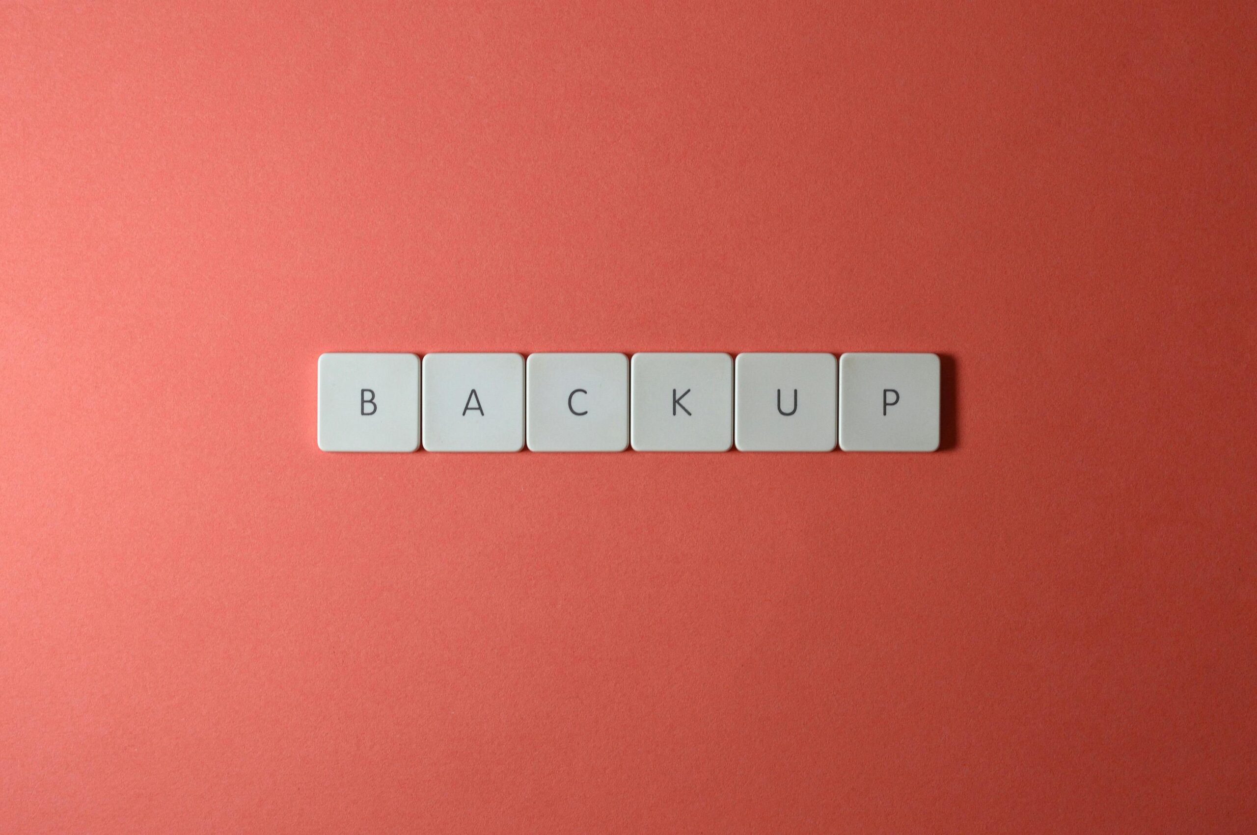 Backup and Recovery Plans Free Close-up of keyboard keys spelling 'BACKUP' placed on a coral-colored surface. Stock Photo